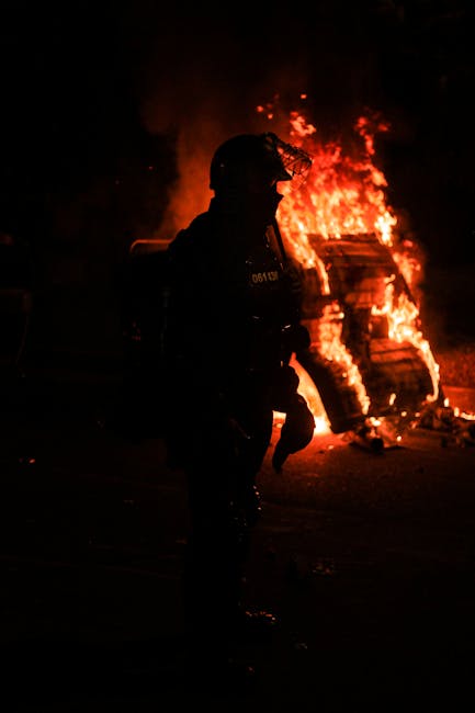 Poliziotto in tenuta antisommossa durante la manifestazione pro-Gaza a Roma del 4 ottobre, con fuoco sullo sfondo e sicurezza rinforzata.