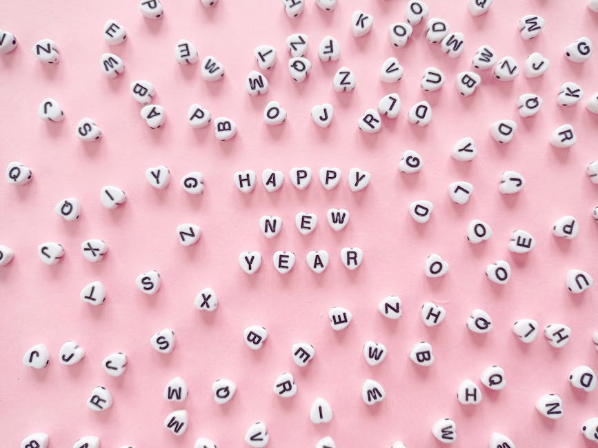 Parole dell'anno 2024: Dettaglio di perline con lettere che compongono la scritta Happy New Year su sfondo rosa, concetto di novità e linguaggio.