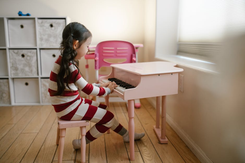 Bambina che suona il pianoforte giocattolo in pigiama a righe, attività di educazione musicale per bambini, apprendimento musicale precoce.