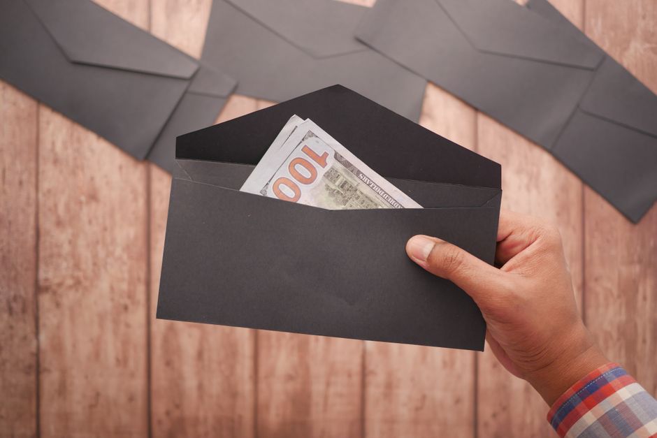 Mano che tiene una busta nera con banconote da 100 dollari, simboleggiando il bonus estivo per docenti e ATA che slitta a settembre