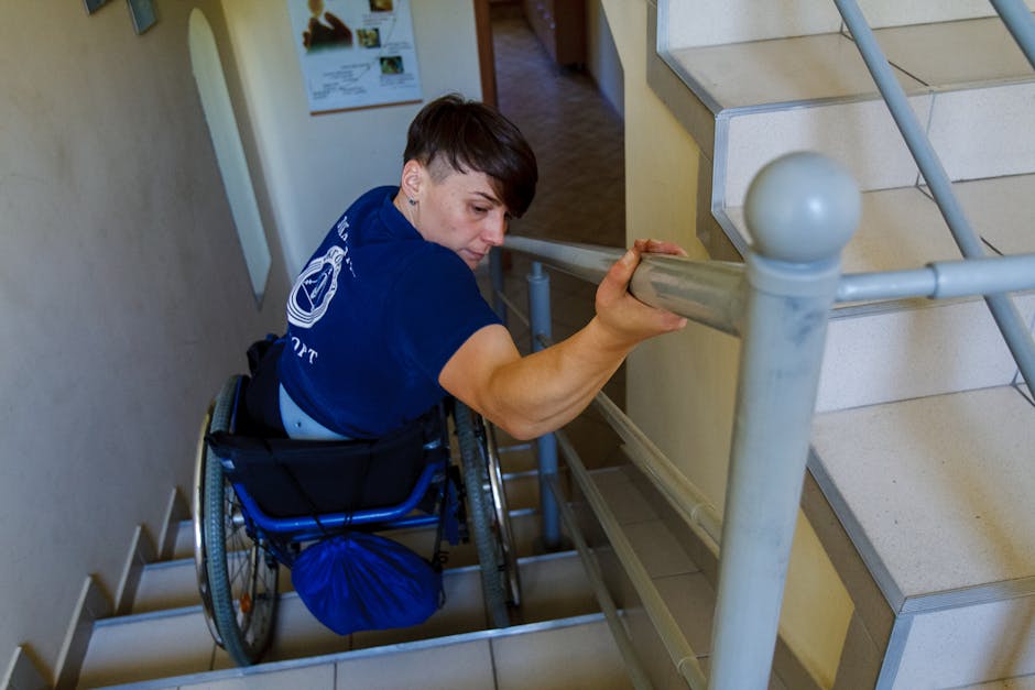 Donna in sedia a rotelle affronta le scale aggrappandosi al corrimano, simbolo di resilienza e diritto all'istruzione nonostante le barriere.