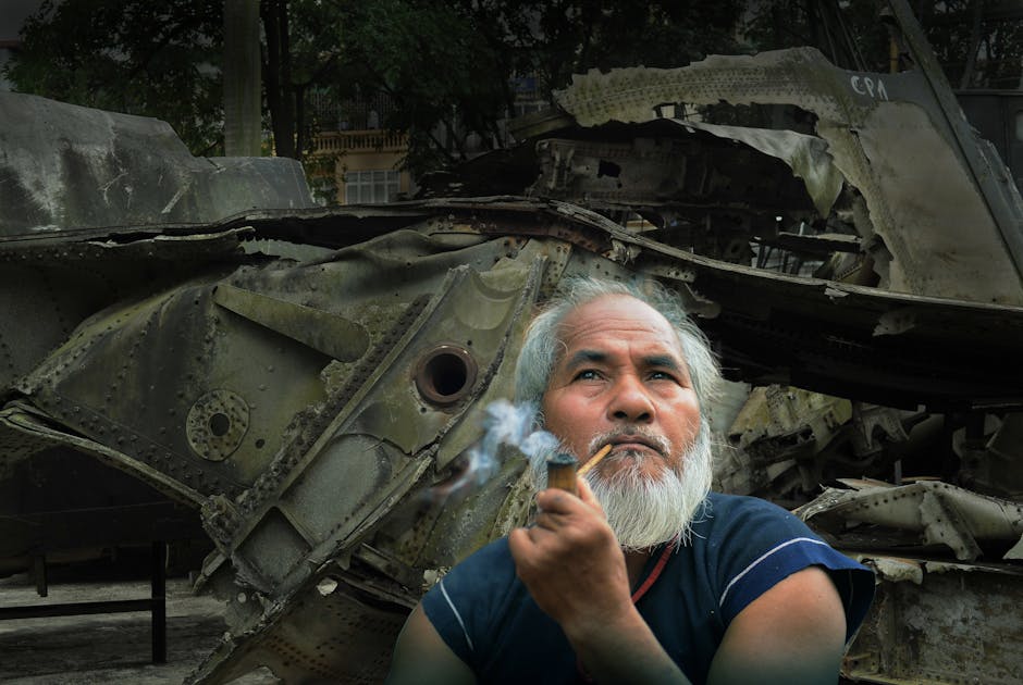 Uomo con pipa davanti a rottami di aereo, simbolo di conflitti e fervore storico, evocativo della Prima Crociata e delle sue battaglie.