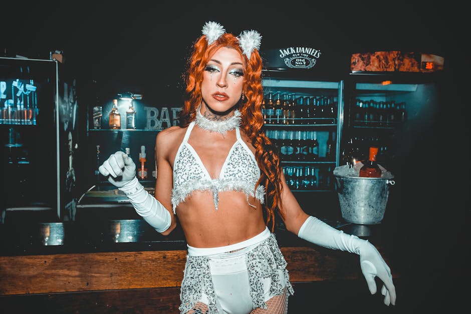 Drag queen con costume scintillante e orecchie da gatto in un bar, espressione seria, possibile evento serale per genitori con Daniele Novara.
