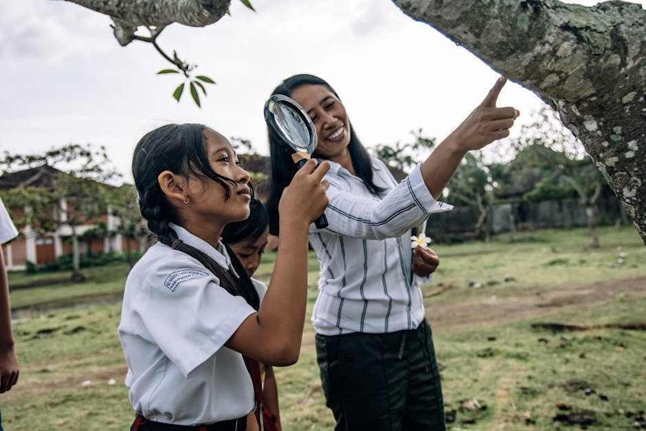 Studentessa di Scienze della Formazione Primaria con lente d'ingrandimento studia la natura con la sua insegnante durante una lezione all'aperto.