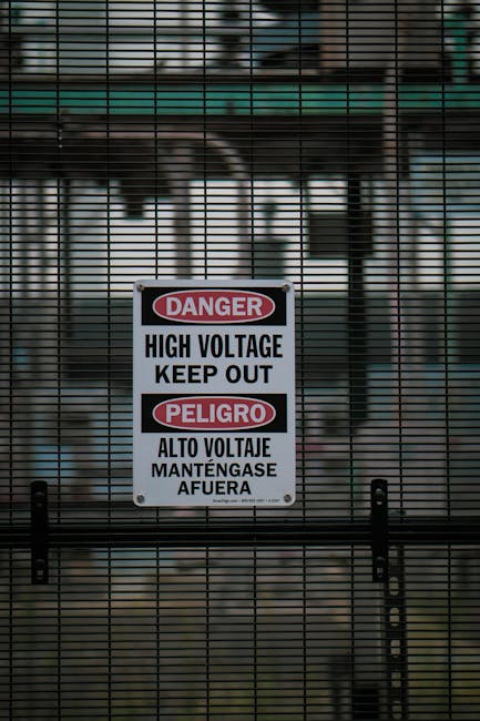 Cartello di pericolo alta tensione in inglese e spagnolo su recinzione metallica, sicurezza linguistica per imparare l'inglese