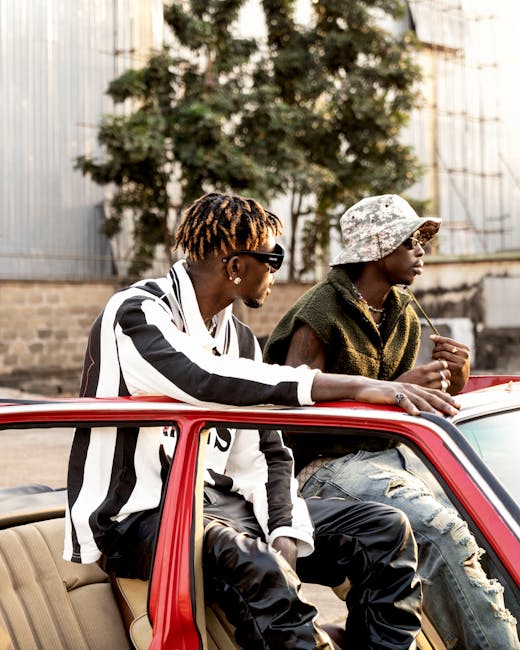 Due giovani musicisti rilassati su un'auto d'epoca, simbolo di creatività e benessere emotivo legato all'ascolto e alla composizione musicale. La loro espressione riflette la gioia e la passione per la musica.