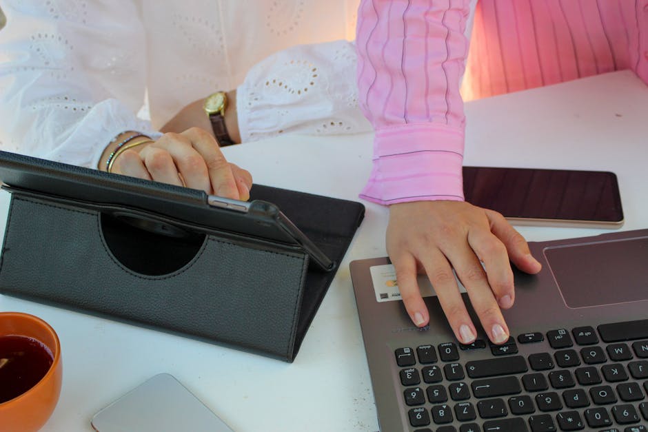 Persona che lavora al computer e tablet per progetti di collaborazione internazionale online, focus su mani e dispositivi digitali.
