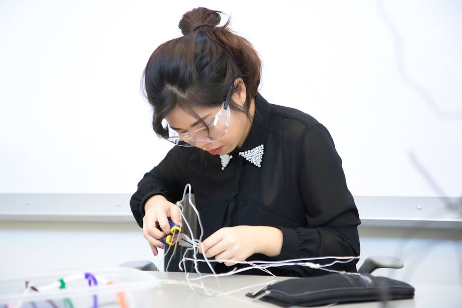 Studentessa con occhiali protettivi utilizza pinze per lavorare su cavi, esempio di apprendimento pratico e tecniche didattiche innovative.