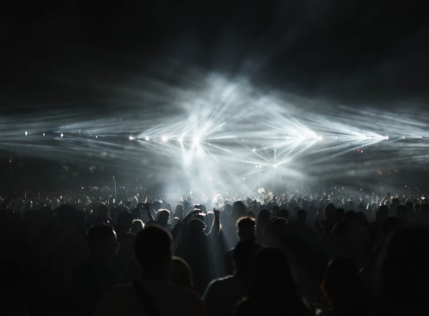 Folla entusiasta a concerto musicale con luci intense e atmosfera coinvolgente, un'esperienza di divertimento senza paragoni per gli amanti della musica.