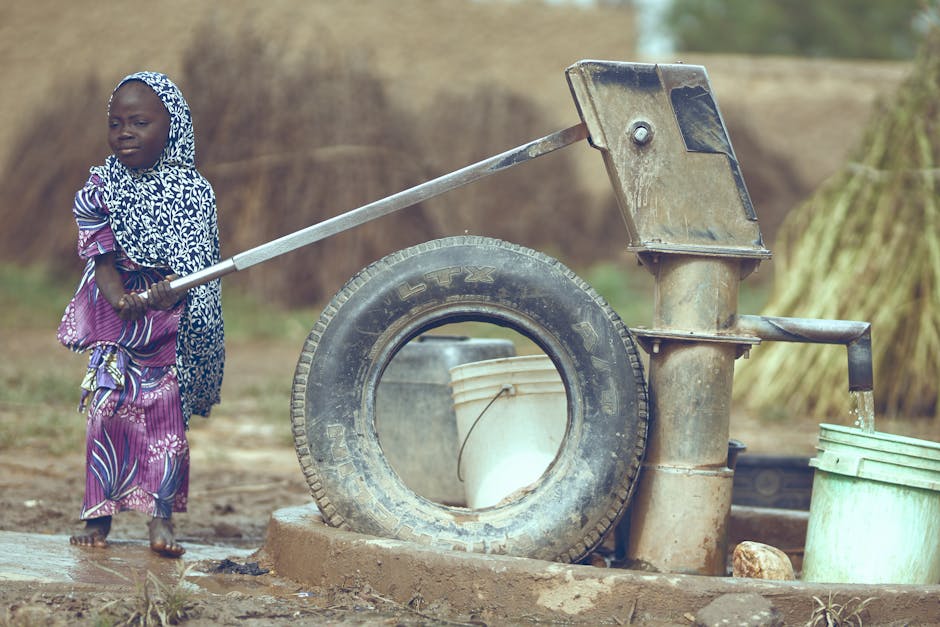 Bambina africana aziona pompa d'acqua manuale: resilienza e speranza per un futuro migliore, simbolo di benessere e forza interiore.
