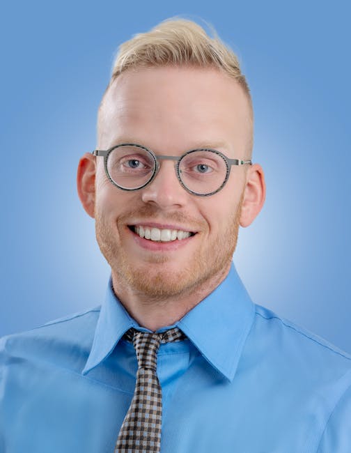 Uomo sorridente con occhiali tondi e camicia azzurra, espressione positiva per un ambiente di lavoro stimolante e accogliente.