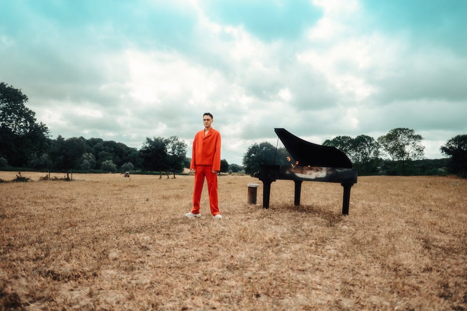 Uomo in abito rosso accanto a pianoforte a coda bruciato in campo arido, metafora della potenza emotiva e distruttiva della musica