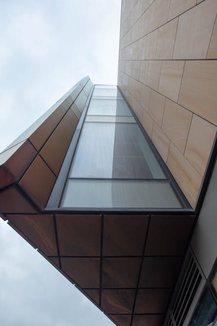 Altezza e geometria: edificio triangolare moderno Edificio moderno con facciata triangolare e vetrata, prospettiva dal basso che enfatizza l'altezza della struttura e la sua forma geometrica.
