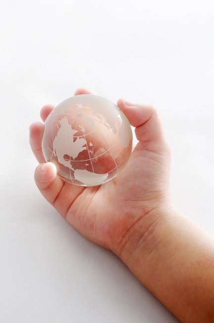 Mano che sorregge un globo di vetro con continenti incisi, simbolo di responsabilità globale e inclusione per il futuro.
