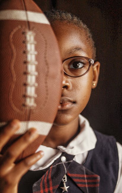 Bambina con occhiali e divisa scolastica tiene un pallone da football, simbolo di talento e potenziale unico nell'apprendimento.