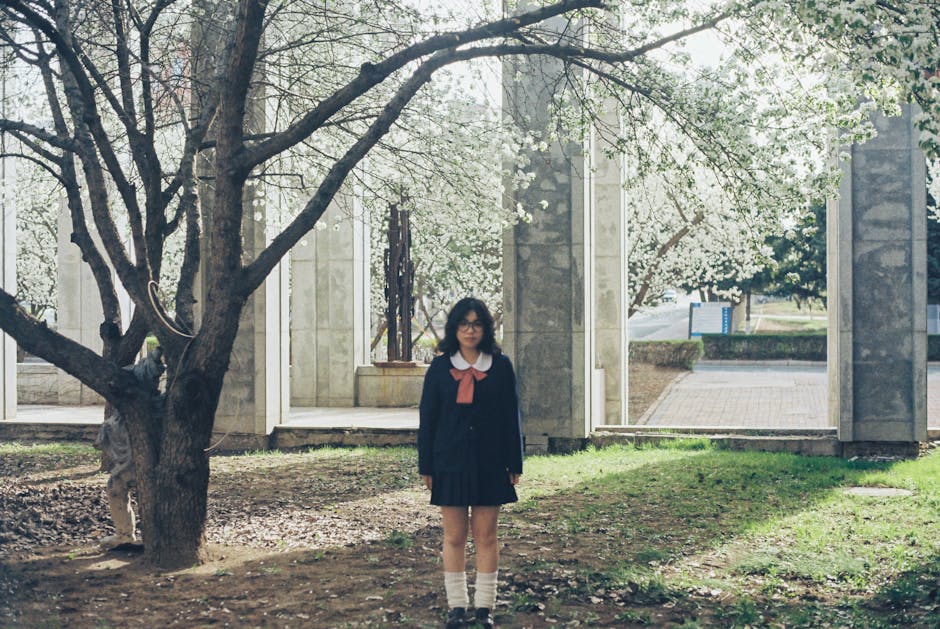 Studentessa in divisa scolastica tra gli alberi in fiore, contesto sindacale FLC CGIL e rinnovo contratti scolastici con aumenti insufficienti.