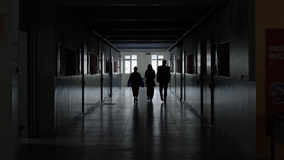 Corridoio ospedaliero con figure in ombra, riflesso della situazione psicologica del docente sospeso dopo il post su Meloni