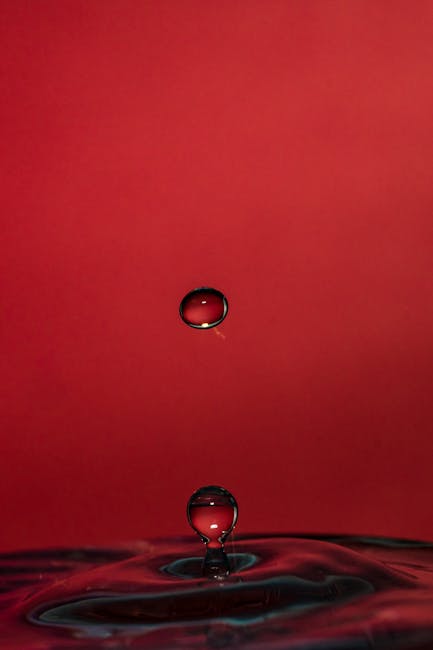 Goccia d'acqua sospesa che ricorda la forma di un triangolo isoscele, design ispirato alla geometria, sfondo rosso intenso.