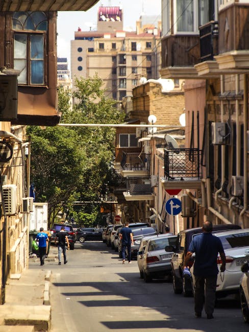Strada cittadina con persone che camminano e auto parcheggiate, architettura urbana che evoca l'atmosfera di Parigi per la danza francese.