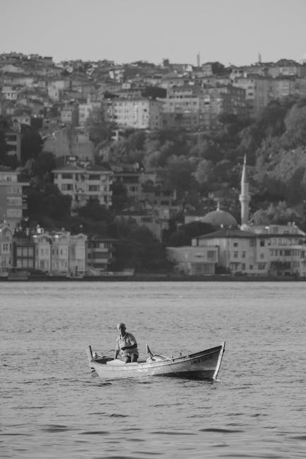 Uomo su barca a remi con città sullo sfondo, immagine in bianco e nero che evoca la ricerca di autorealizzazione.