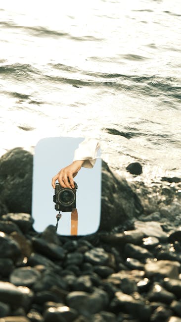 Riflesso di una fotocamera in uno specchio sulla spiaggia, evocando il realismo magico e la percezione alterata della realtà.