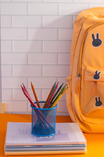 Zaino scolastico giallo con adesivi coniglietto, matite colorate e quaderni. Rischio oggetti pericolosi nelle scuole.