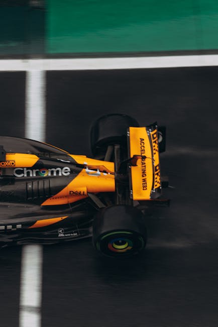 Auto da corsa arancione e nera in movimento, concetto di velocità angolare e movimento rotatorio in Formula 1.