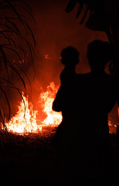 Incendio vicino scuola Mulinu Becciu: silhouette di persona con bambino di fronte alle fiamme, emergenza e paura per i residenti.