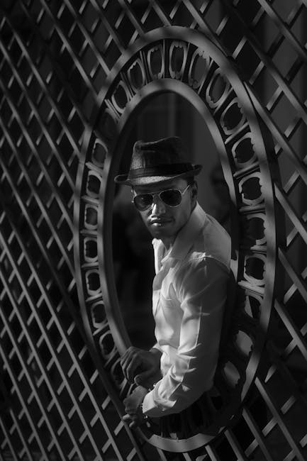 Uomo con cappello e occhiali da sole attraverso una grata circolare, richiamo visivo alle forme geometriche dell'articolo.