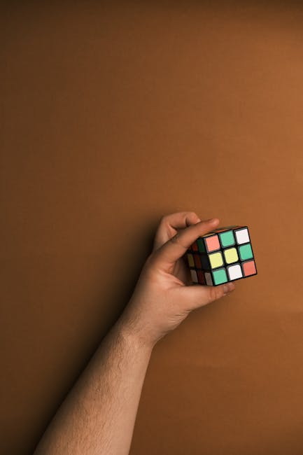 Mano che tiene un cubo di Rubik colorato su sfondo marrone, oggetto manipolativo per rendere la matematica divertente e accessibile.