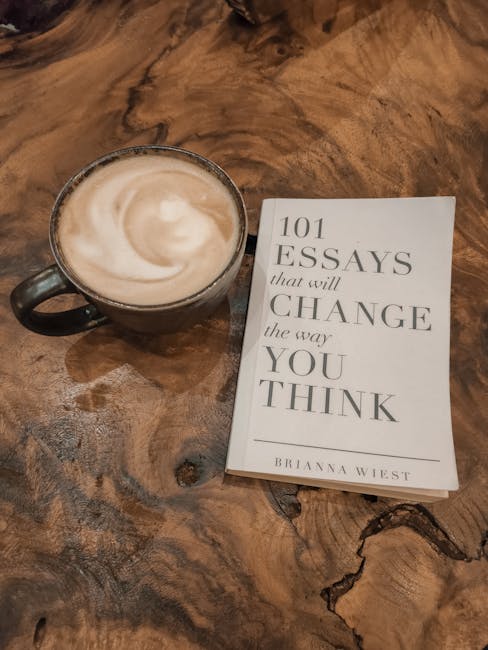 Tazza di cappuccino e libro '101 Essays that will change the way you think' su tavolo di legno, metafora della lettura e introspezione sensoriale