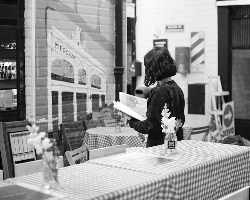 Donna legge seduta a un tavolo con tovaglia a quadri in un locale con murales, ideale per comfort e funzionalità unici.