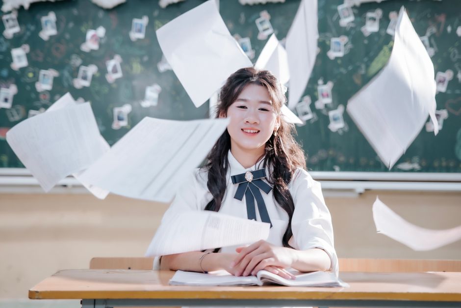 Studentessa sorridente con fogli volanti, PC ricondizionati per la scuola e Carta del Docente Reware