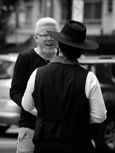 Uomo con occhiali che parla con persona con cappello, espressione di certezza nel dialogo quotidiano, foto in bianco e nero.