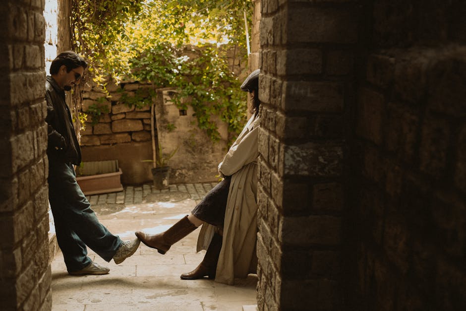 Uomo e donna appoggiati a muri di pietra in vicolo soleggiato, metafora visiva di legami e connessioni, area e circonferenza