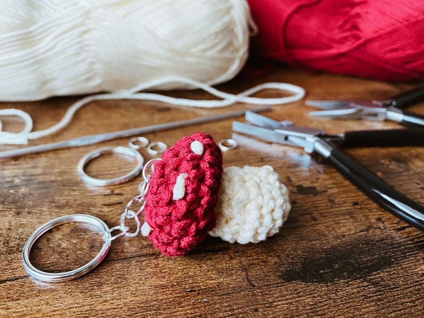 Portachiavi a forma di fungo amigurumi fatto a mano con uncinetto e filato rosso e bianco, strumenti per l'artigianato su tavolo di legno.