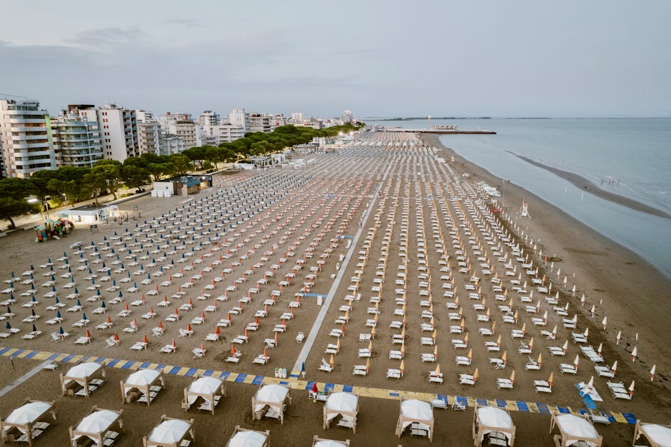Vista aerea della spiaggia di Lignano Sabbiadoro con ombrelloni e lettini, contesto gita scolastica e incidente allo studente