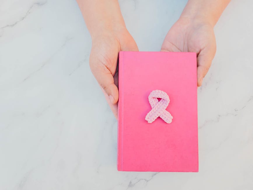 Mani che sostengono un libro rosa con un fiocco rosa all'uncinetto, simbolo della lotta contro il tumore al seno.