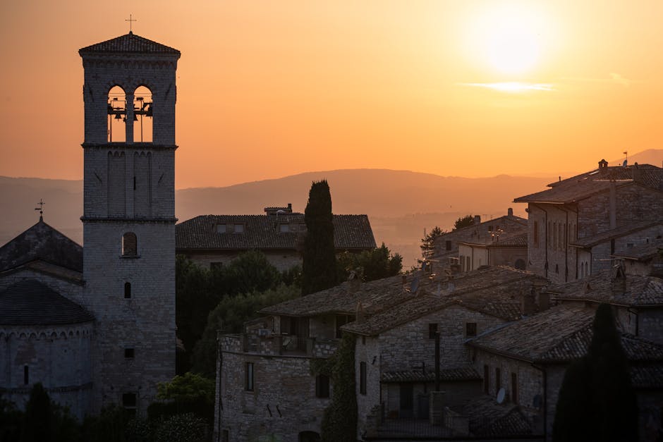 Assisi al tramonto: campanile, case in pietra e cielo arancione. Festa nazionale di San Francesco d'Assisi il 4 ottobre.