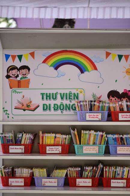 Scaffali pieni di libri per bambini con un arcobaleno e disegni di bambini su uno sfondo, che rappresentano la biblioteca scolastica mobile del progetto Ioleggoperché.