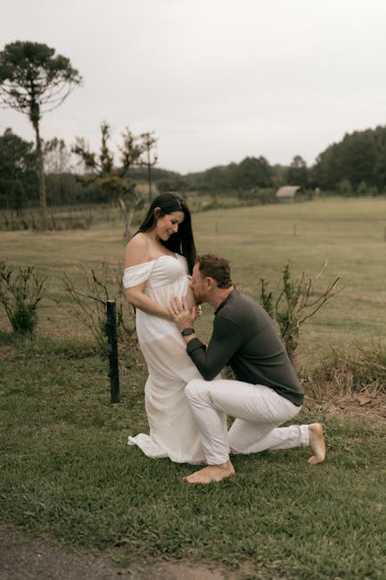 Uomo che bacia il pancione di una donna incinta in abito bianco, simbolo di affetto e legame familiare, equilibrio emotivo nella genitorialità.