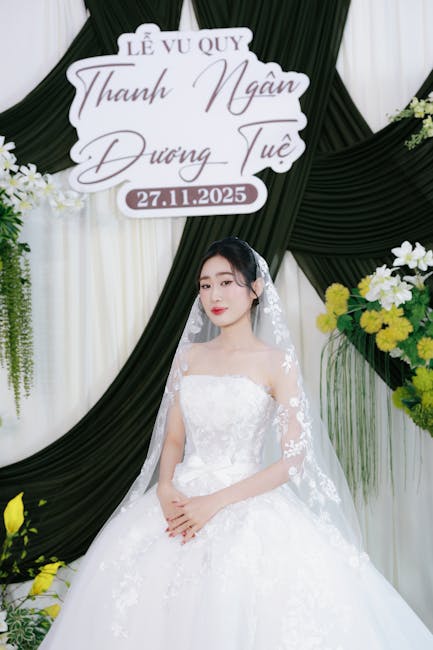 Sposa in abito bianco con velo, cerimonia nuziale con data 27 novembre 2025 sullo sfondo, decorazioni floreali e drappeggi.