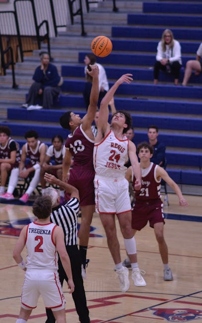 Partita di basket scolastica: giocatori in elevazione per la palla a due, arbitro in primo piano. Promozione sportiva nelle scuole.