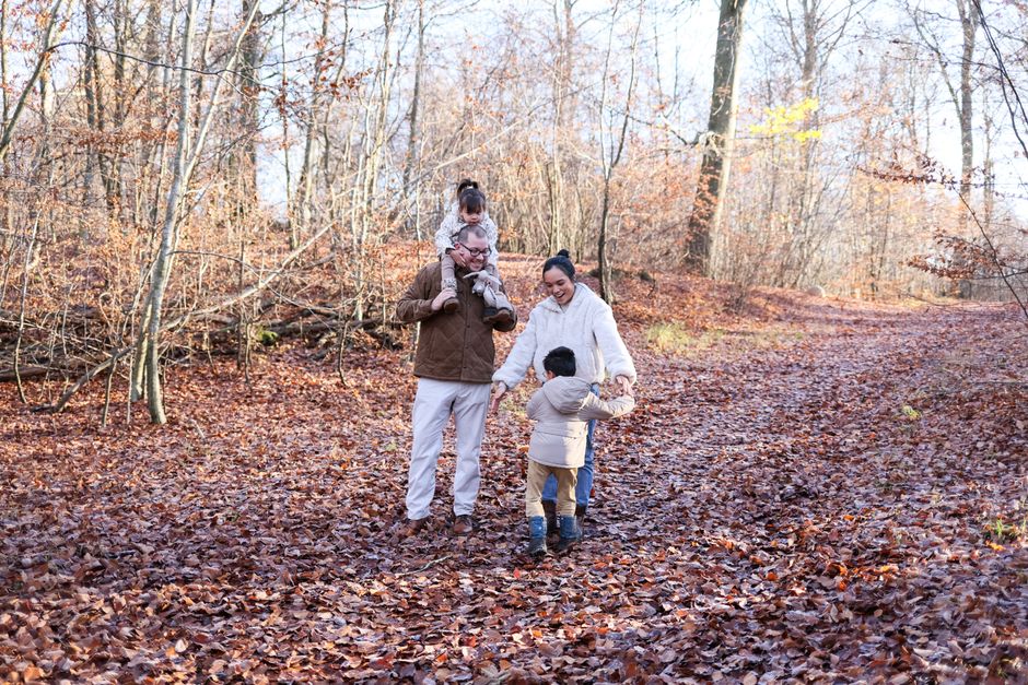 Famiglia nel bosco con bambini, uno sulle spalle del padre, in un contesto che richiama la discussione sull'obbligo scolastico e vaccinale.