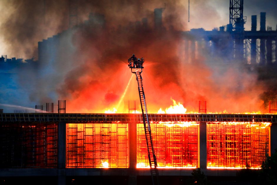 Vigili del fuoco combattono un incendio in un edificio in costruzione, con fiamme alte e fumo denso che avvolgono la struttura, evidenziando i rischi strutturali.