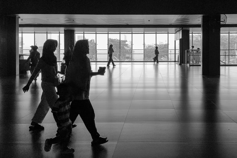 Silhouettes di persone che camminano in un edificio moderno con grandi finestre, metafora della mobilità dei dirigenti scolastici verso il 2026.