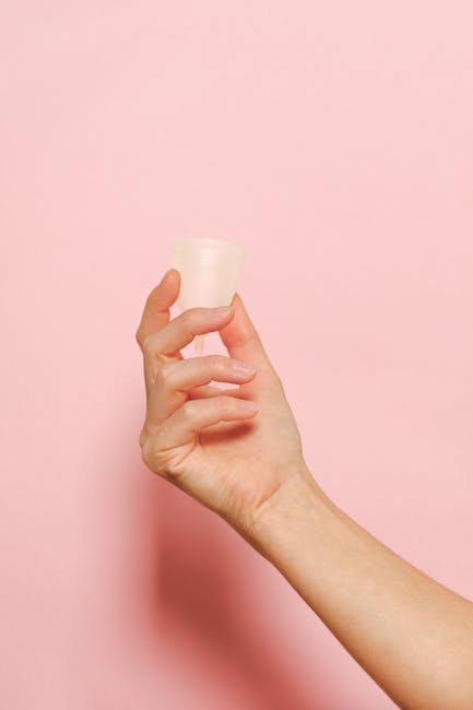 Mano che tiene una coppetta mestruale in silicone su sfondo rosa, esempio di materiale formativo accessibile per l'educazione sessuale.