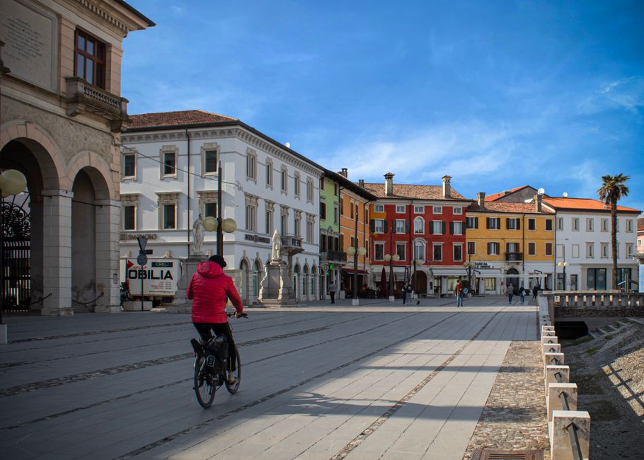 Piazza con edifici colorati e persona in bicicletta, simbolo di attività extrascolastiche finanziate dal bando Friuli Venezia Giulia