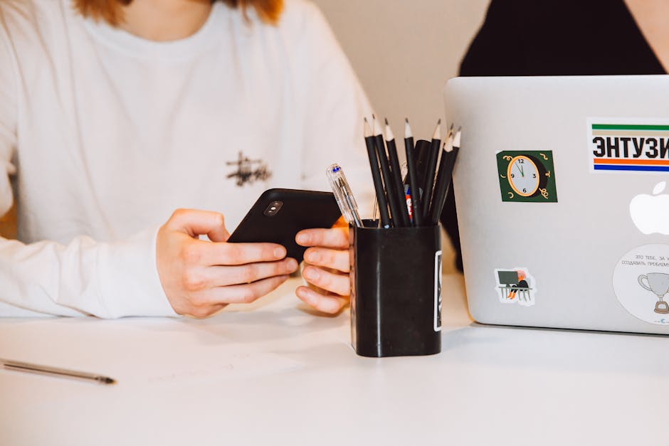 Studente usa il cellulare a scuola nonostante il divieto, con astuccio magnetico e laptop sullo sfondo, concentrazione e tecnologia