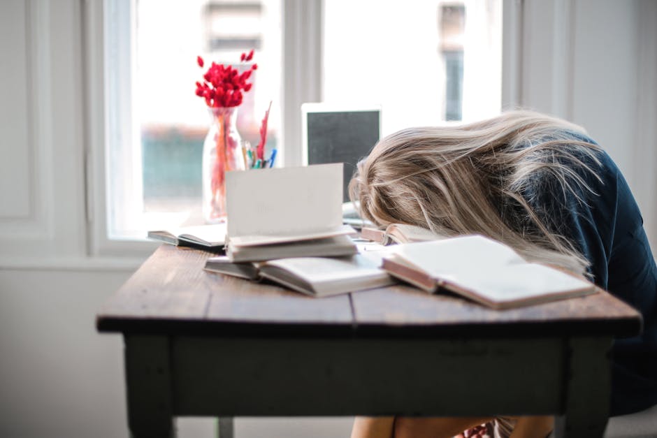 Docente esausta appoggiata alla scrivania con libri, simbolo del burnout e dell'emergenza educativa tra gli insegnanti italiani.